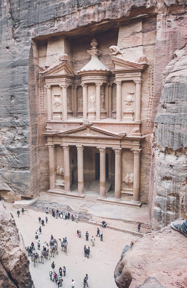 Aerial view of the Treasury with a hiker, solo traveler, young man tourist on a cliff after reaching the top, Al Khazneh in the ancient city of Petra, Jordan, UNESCO World Heritage Site