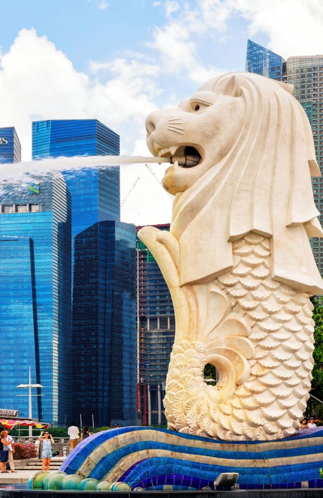 Singapore, Singapore - March 1, 2016: Merlion statue spraying the water out of its mouth at Merlion Park in Downtown Core of Singapore at Marina Bay. Skyscrapers on the background.